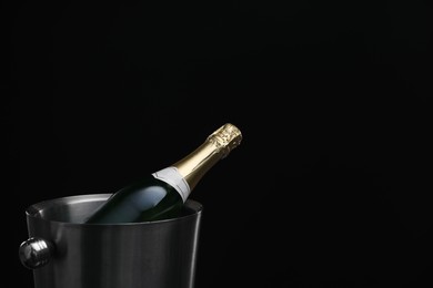 Photo of Bottle of champagne in bucket on black background, space for text