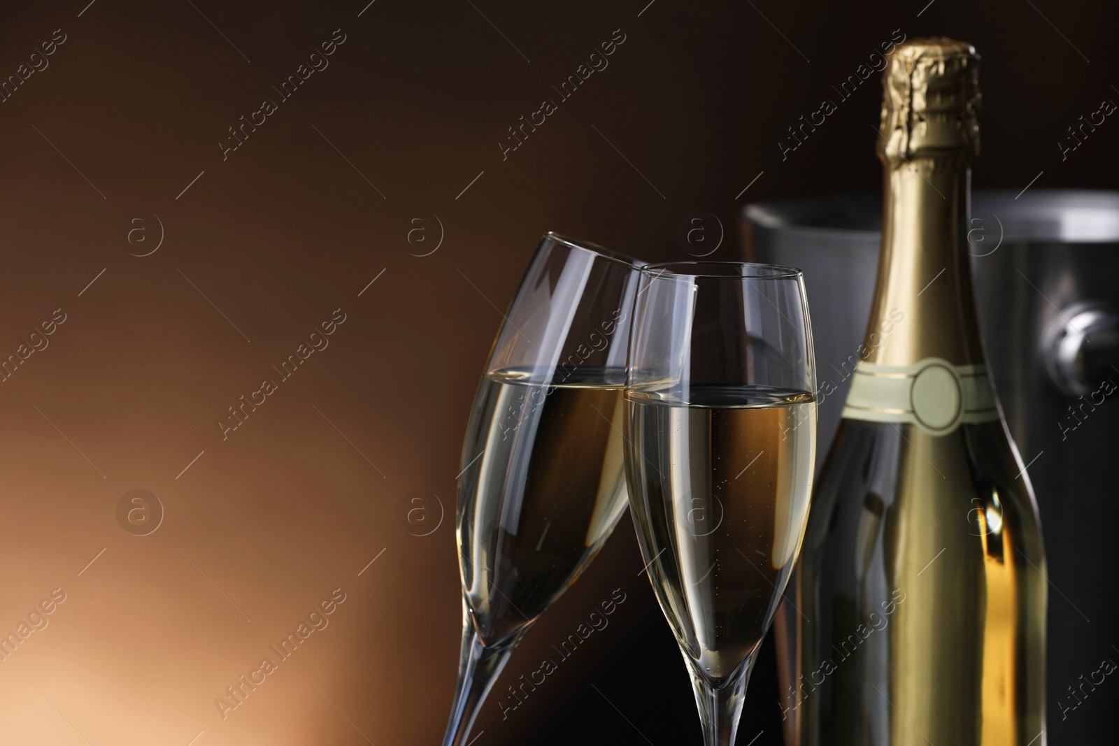 Photo of Champagne in glasses and bottle on brown background, space for text