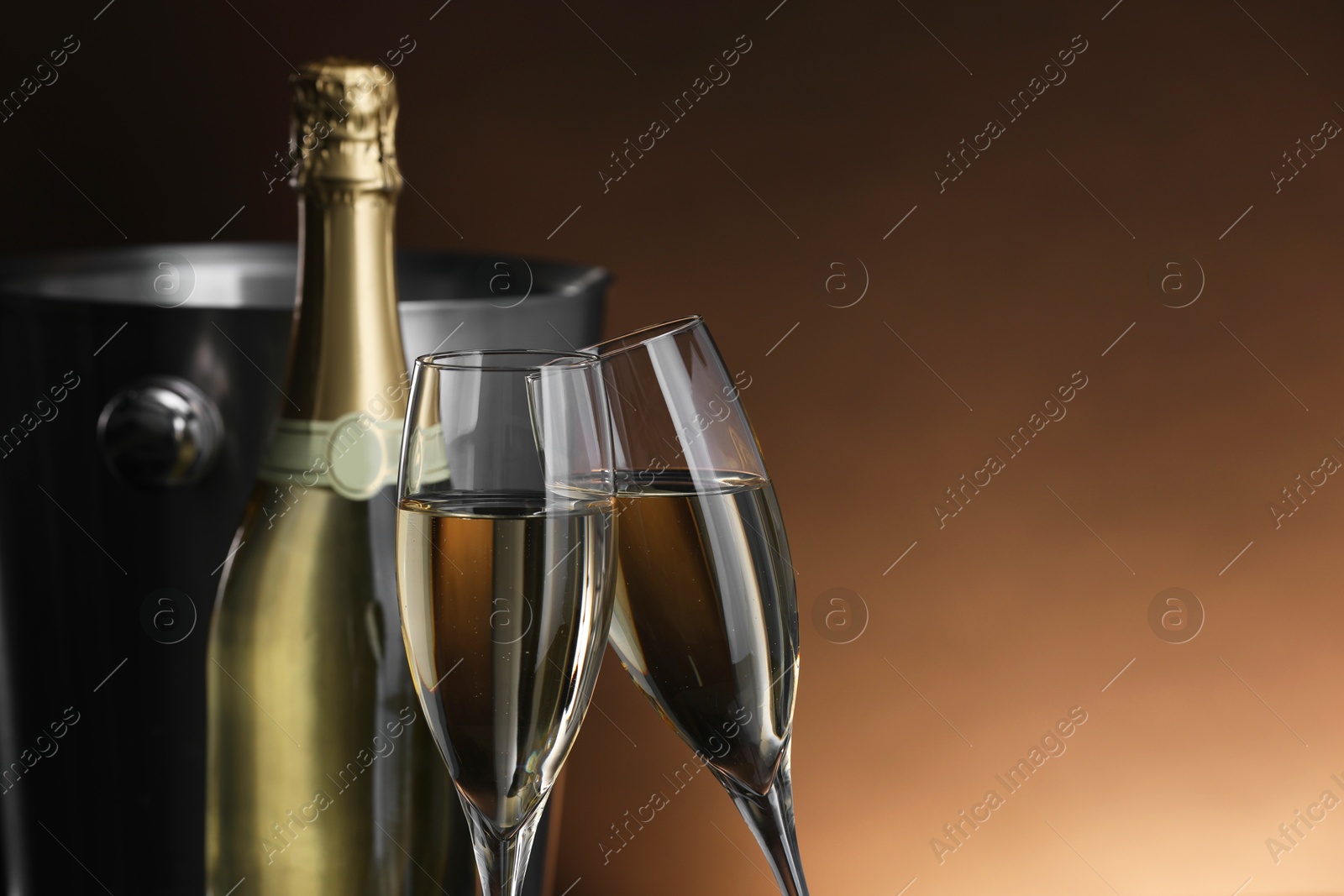 Photo of Champagne in glasses and bottle on brown background, space for text