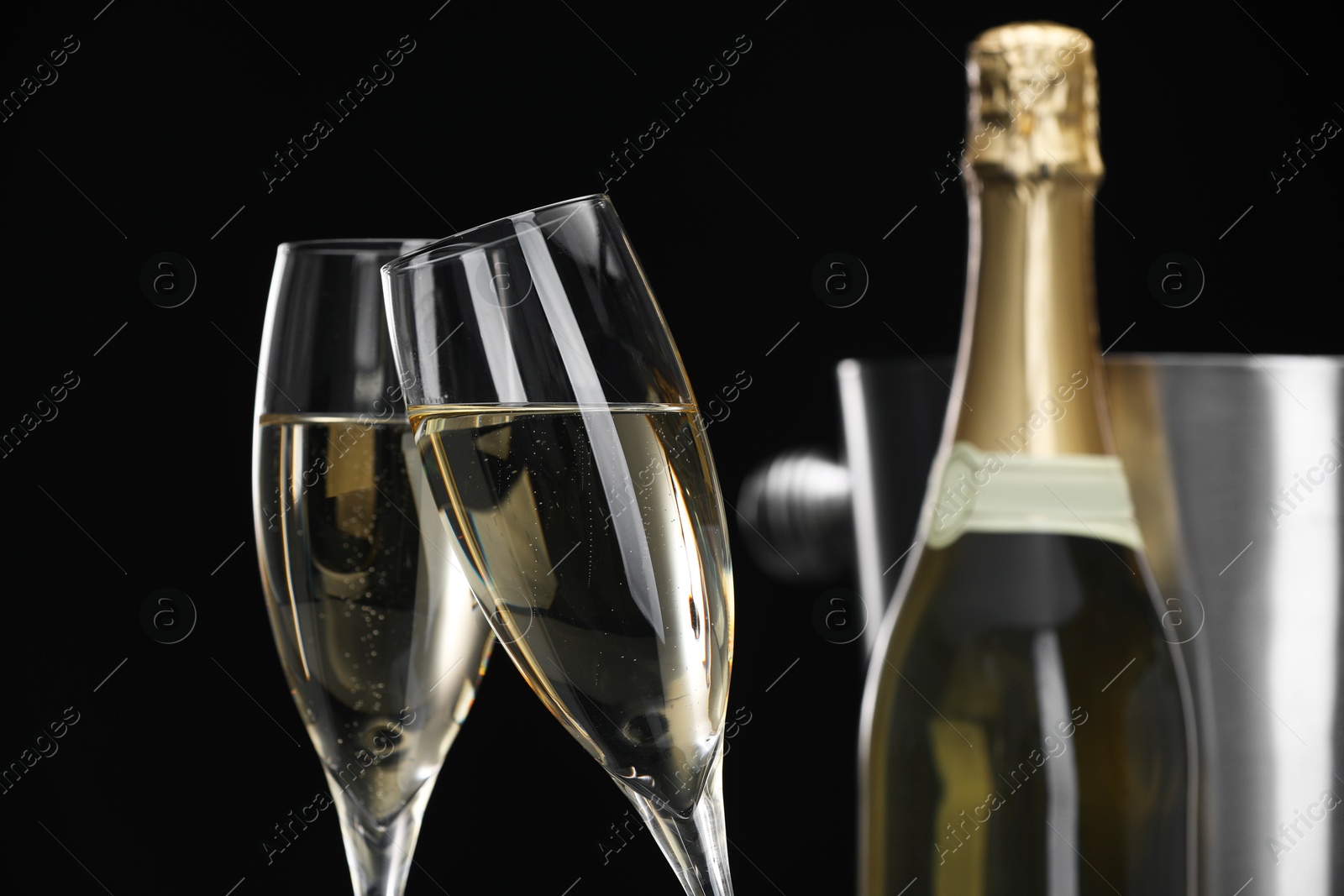 Photo of Champagne in glasses and bottle on black background, closeup