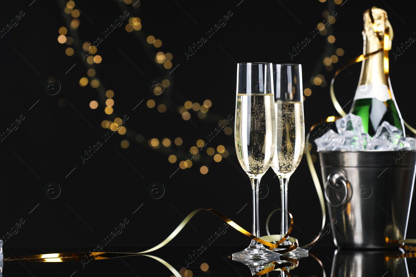 Photo of Champagne and bucket of ice on mirror surface against black background with blurred lights, space for text