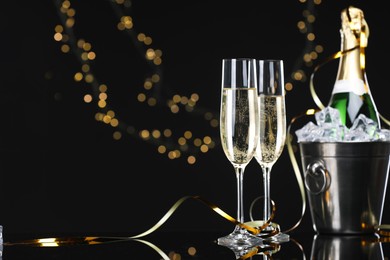 Photo of Champagne and bucket of ice on mirror surface against black background with blurred lights, space for text