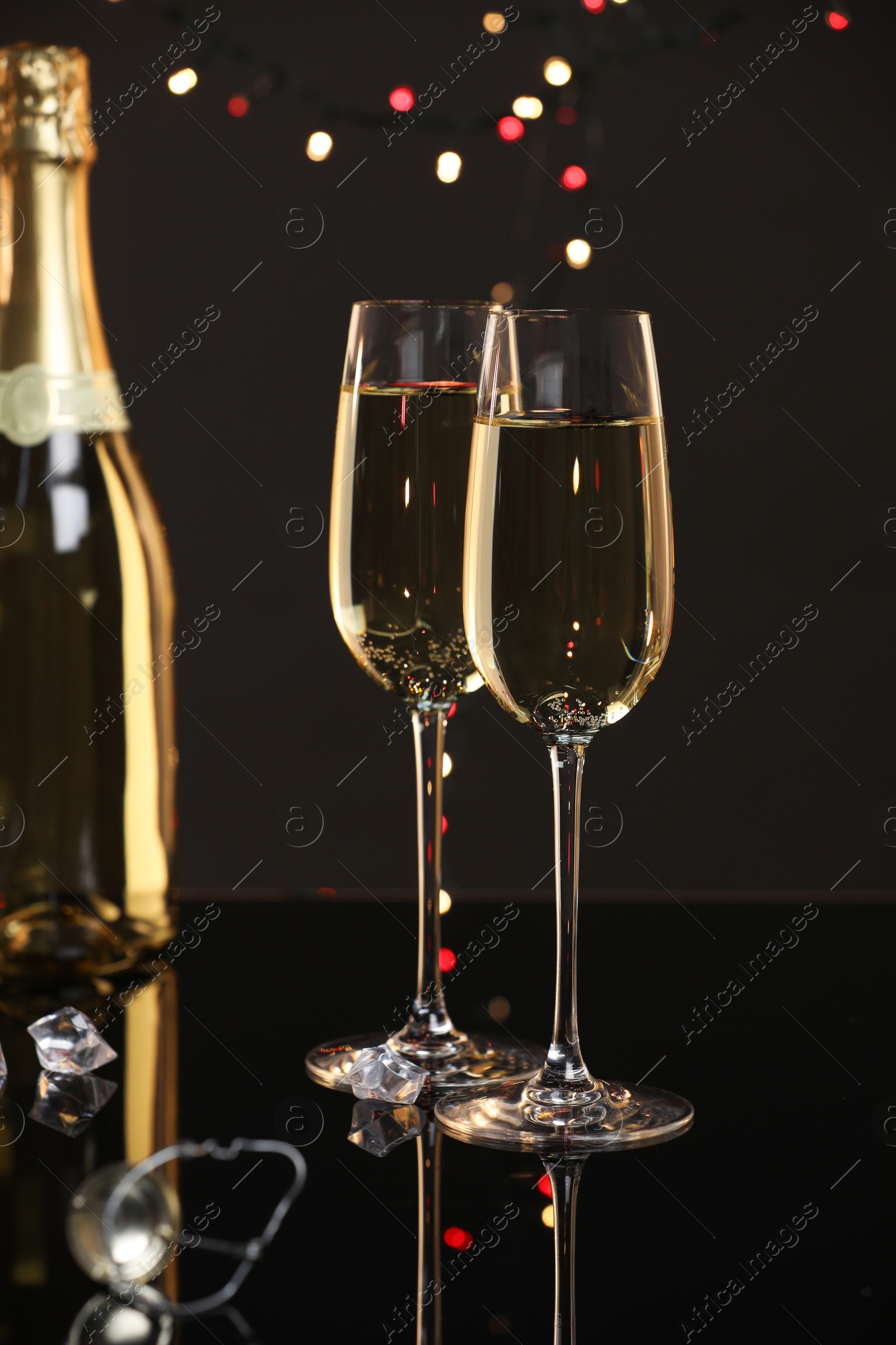 Photo of Champagne in glasses and bottle on black mirror surface