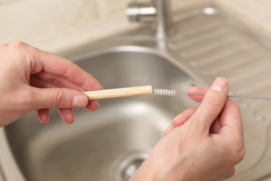 Photo of Woman cleaning bamboo drinking straw with brush in kitchen, closeup