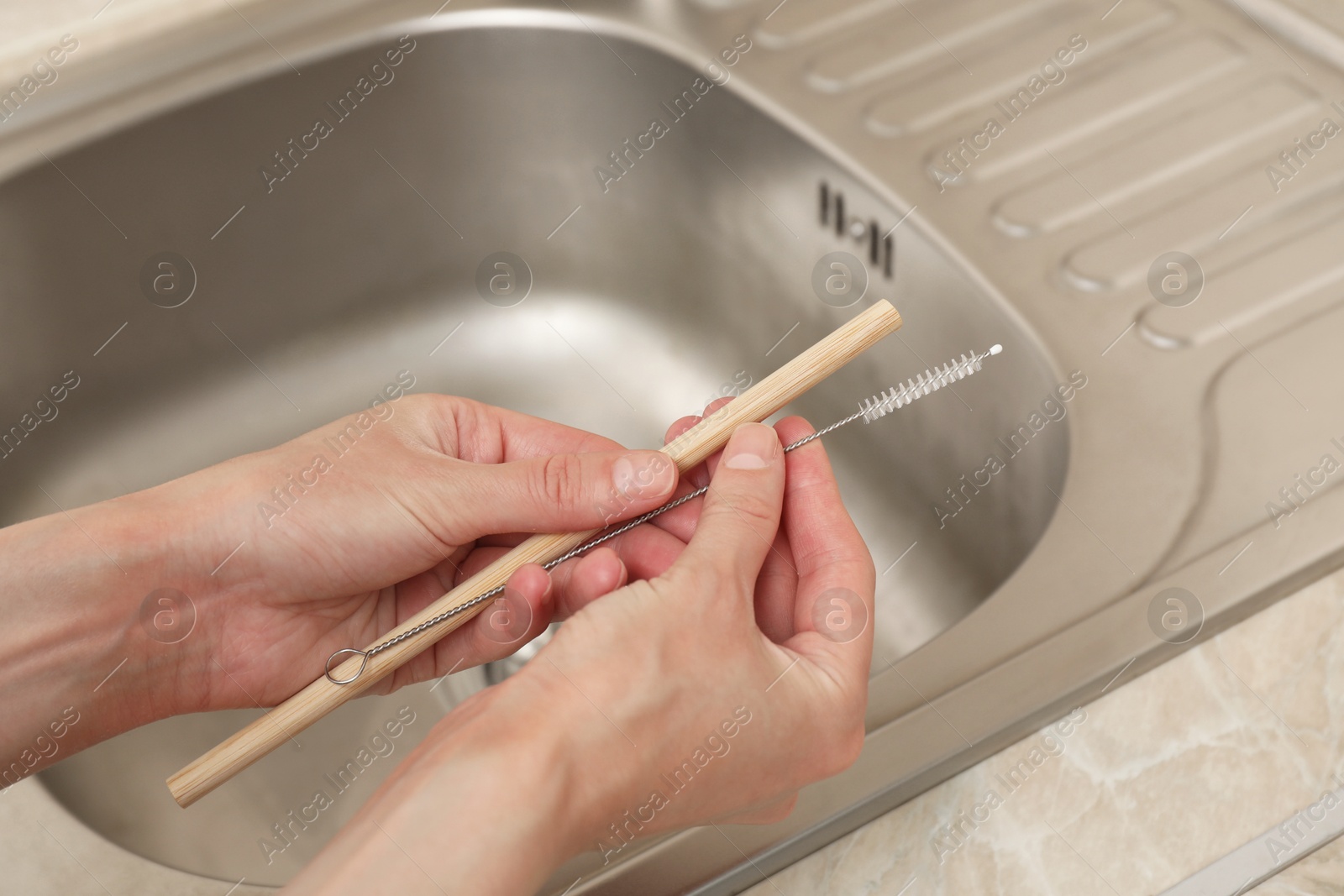 Photo of Woman cleaning bamboo drinking straw with brush in kitchen, closeup