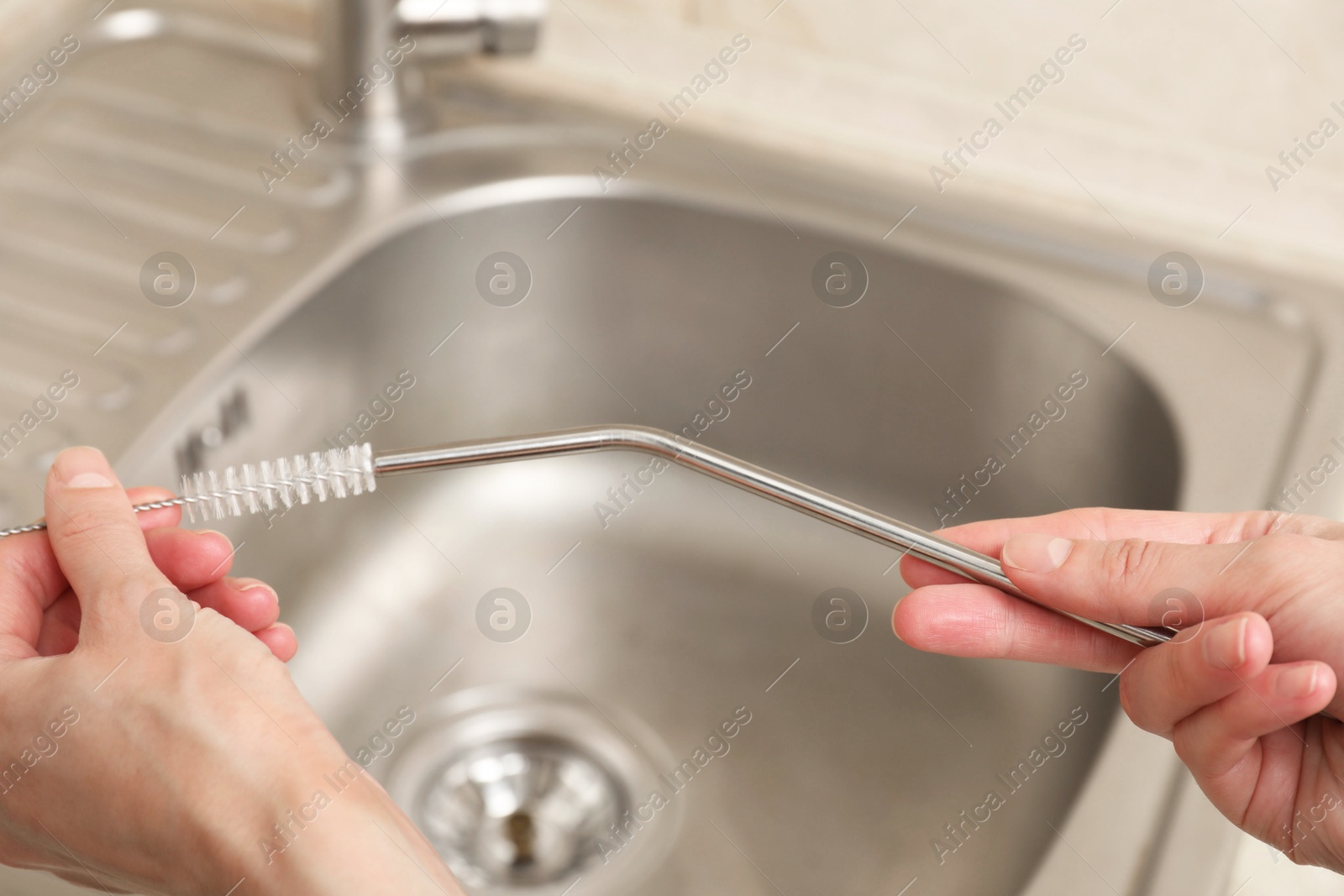 Photo of Woman cleaning metal drinking straw with brush in kitchen, closeup