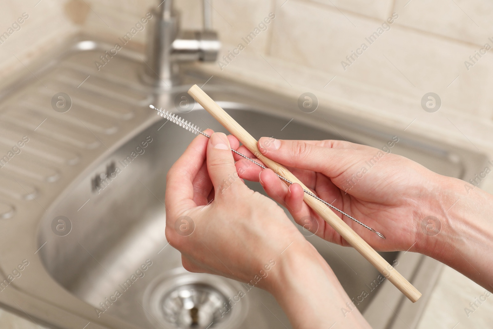 Photo of Woman cleaning bamboo drinking straw with brush in kitchen, closeup