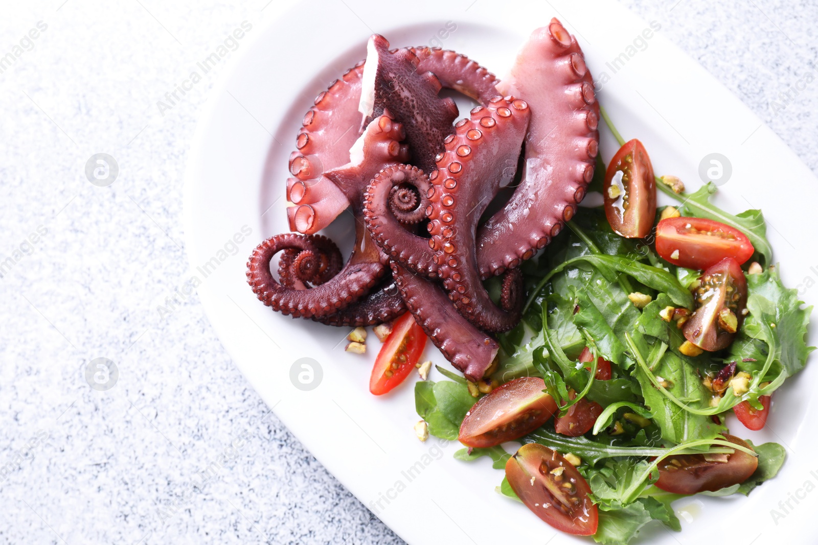 Photo of Plate with tasty boiled octopus tentacles and salad on grey textured table, top view