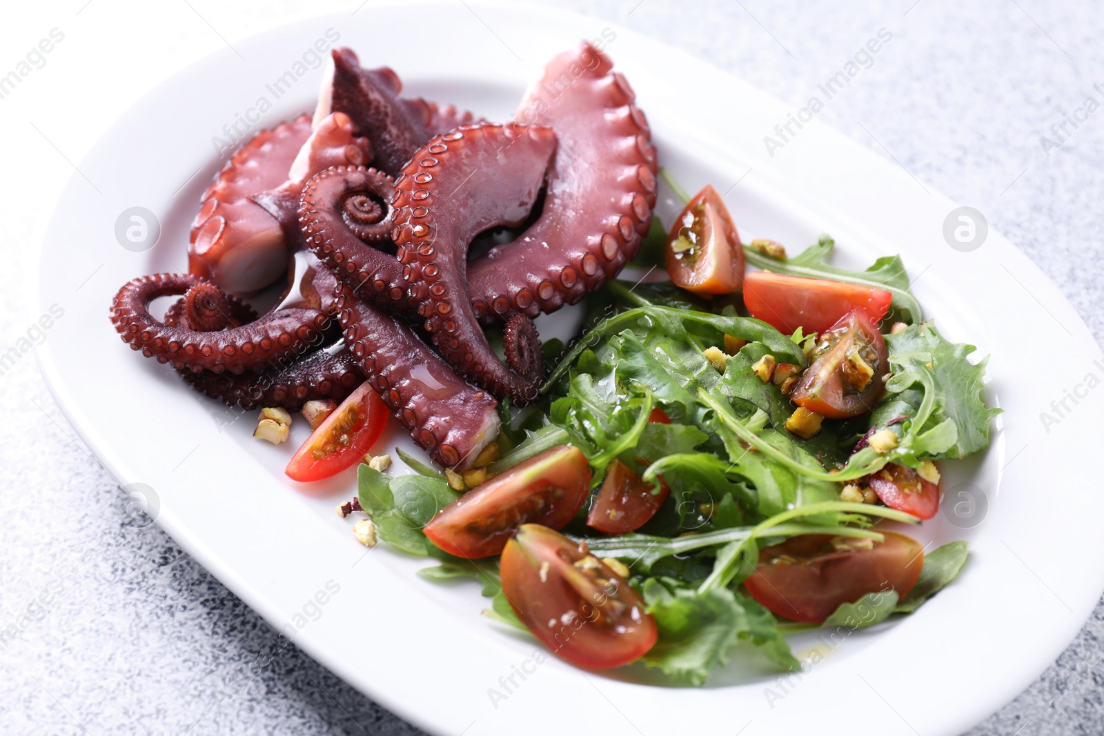 Photo of Plate with tasty boiled octopus tentacles and salad on grey textured table, closeup