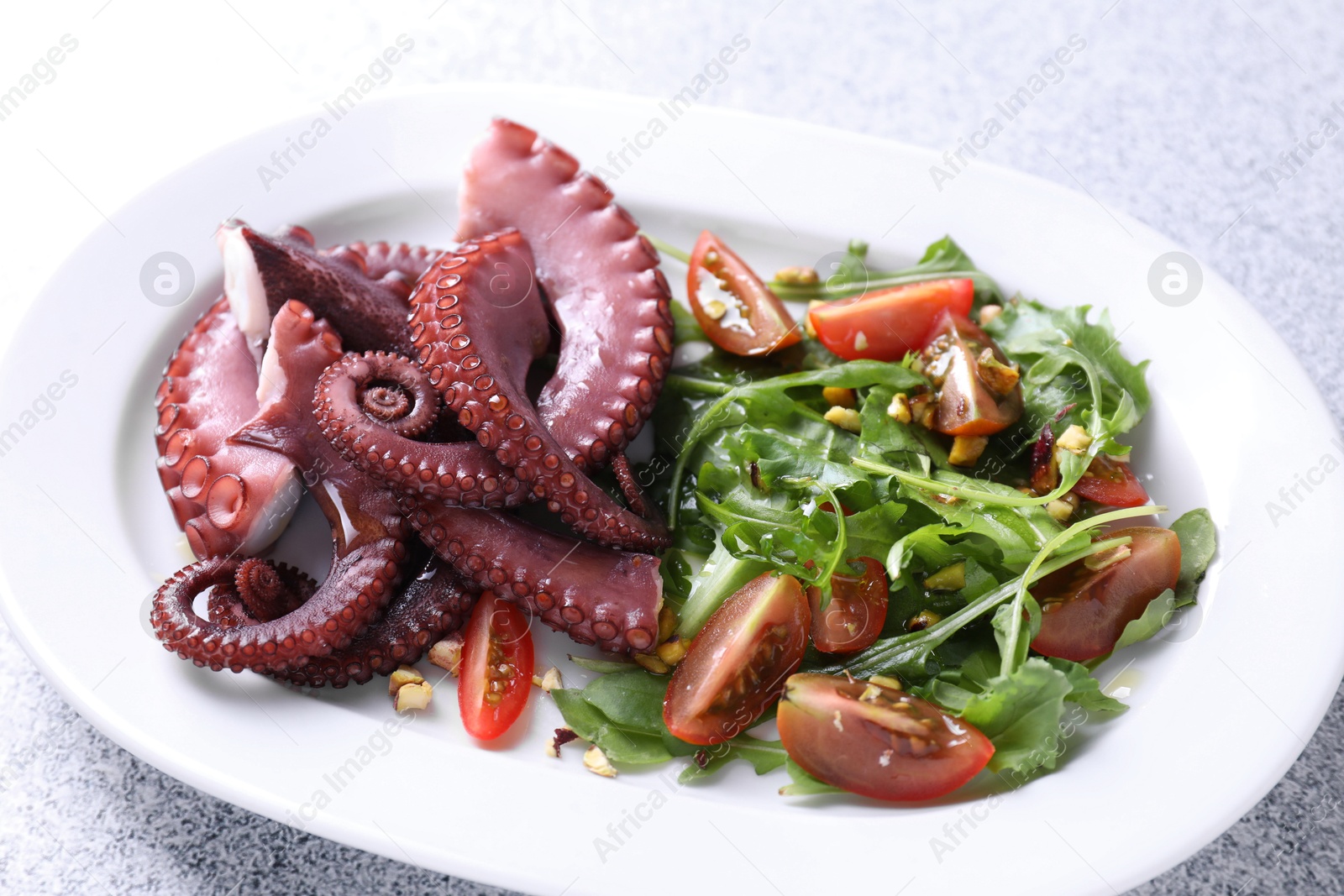 Photo of Plate with tasty boiled octopus tentacles and salad on grey textured table, closeup