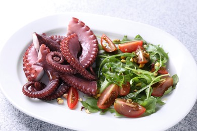 Photo of Plate with tasty boiled octopus tentacles and salad on grey textured table, closeup