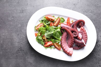 Photo of Plate with tasty boiled octopus tentacles and salad on grey textured table, top view