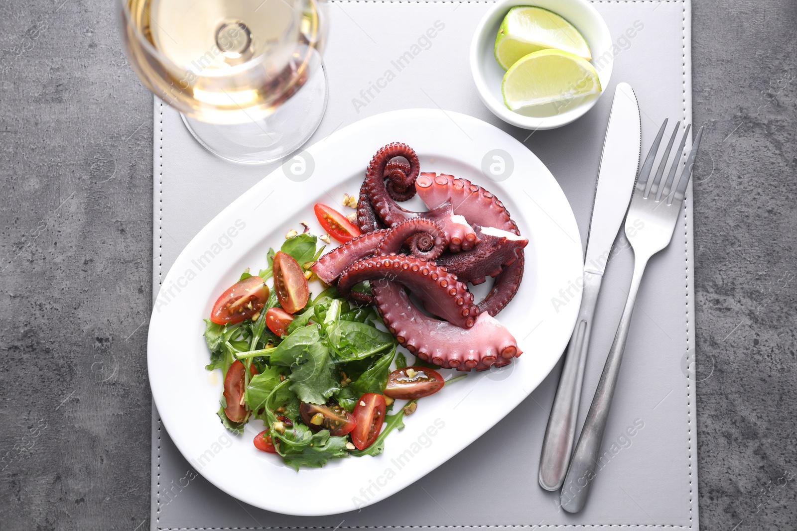 Photo of Plate with tasty boiled octopus tentacles and salad served on grey textured table, top view