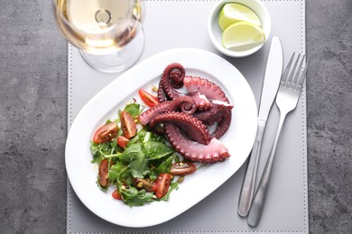 Photo of Plate with tasty boiled octopus tentacles and salad served on grey textured table, top view