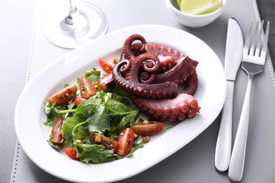 Photo of Plate with tasty boiled octopus tentacles and salad served on grey table, closeup