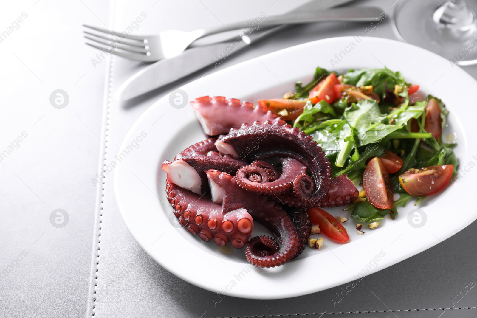 Photo of Plate with tasty boiled octopus tentacles and salad on grey table, closeup