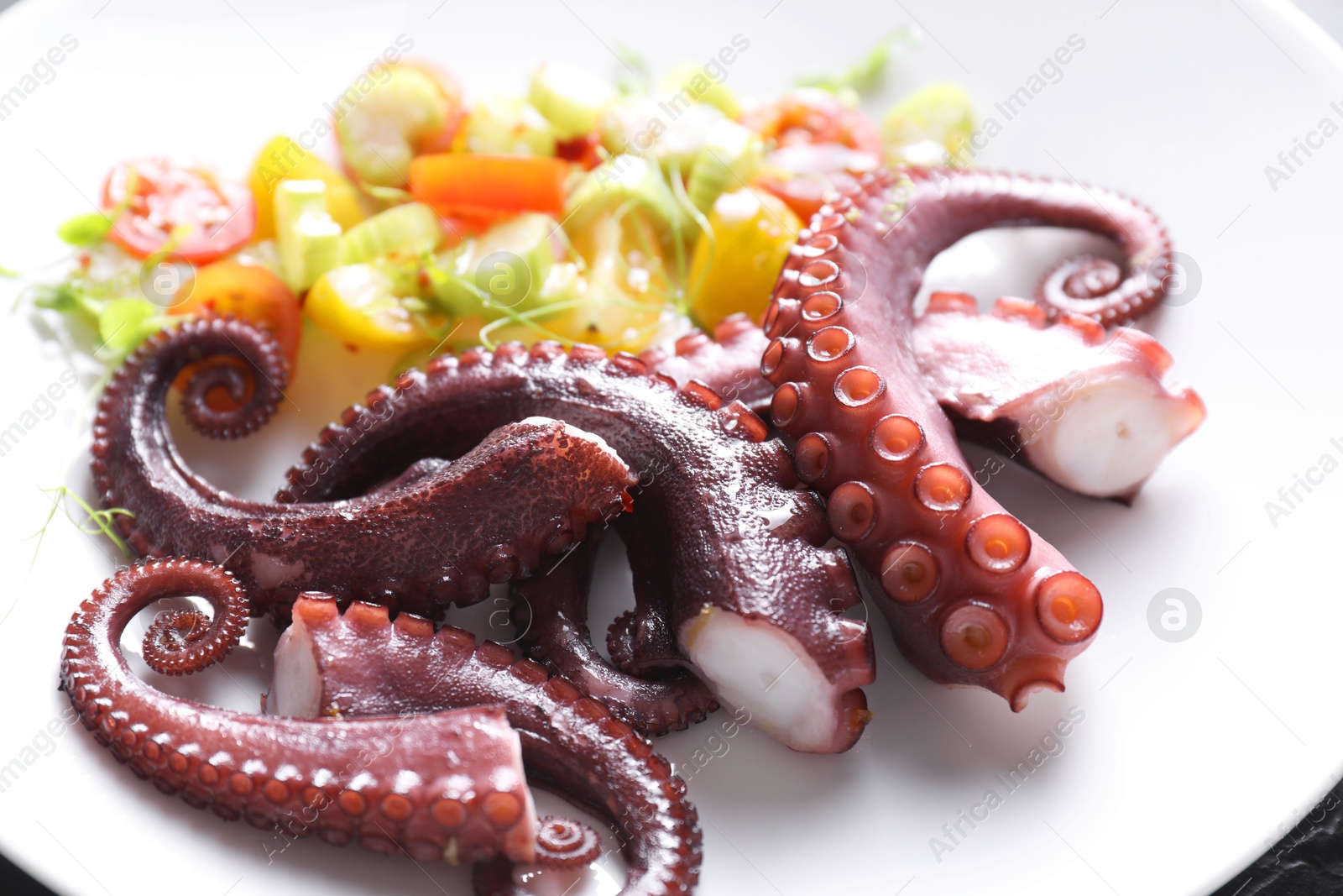 Photo of Tasty boiled octopus tentacles and salad on plate, closeup