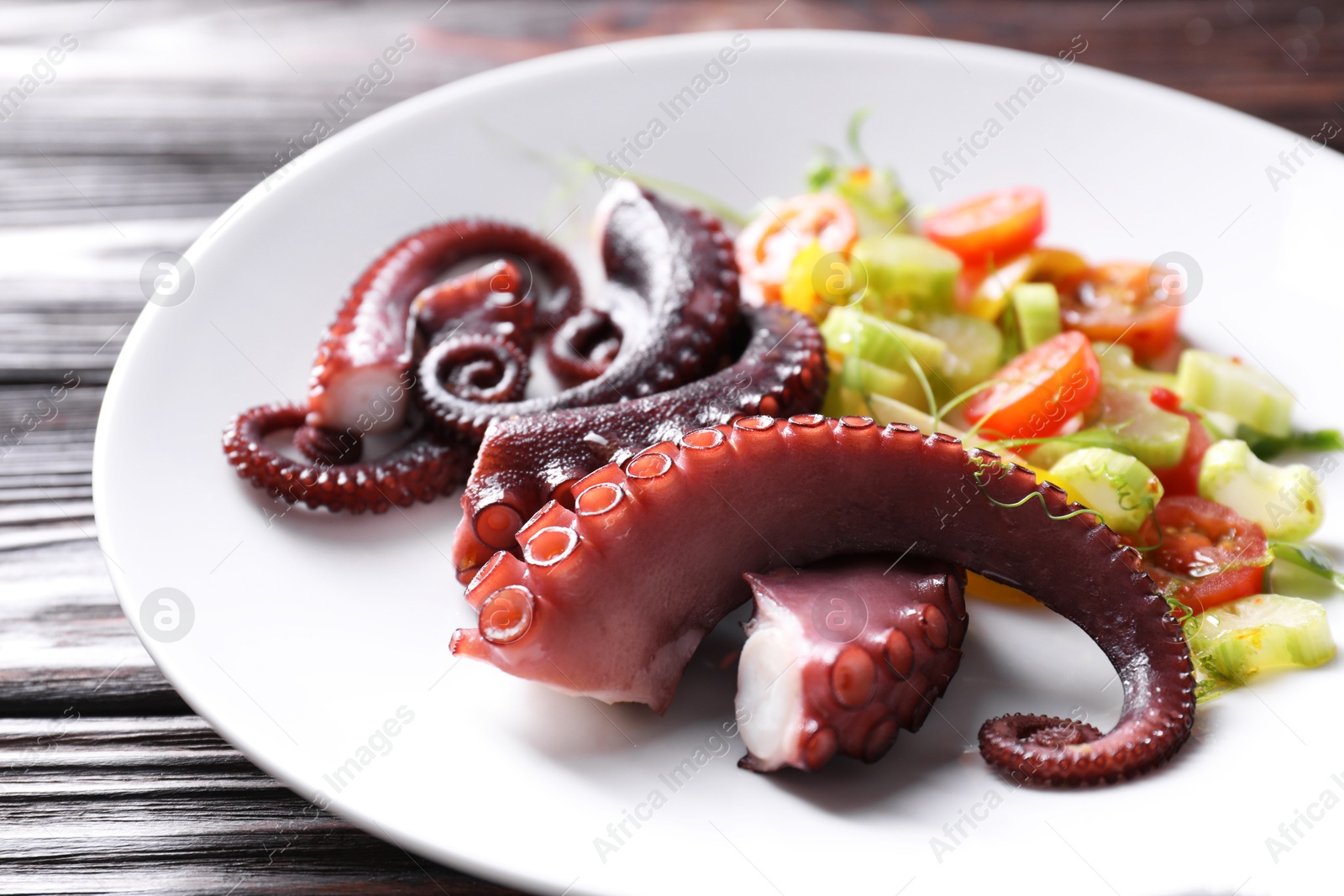 Photo of Plate with tasty boiled octopus tentacles and salad on wooden table, closeup