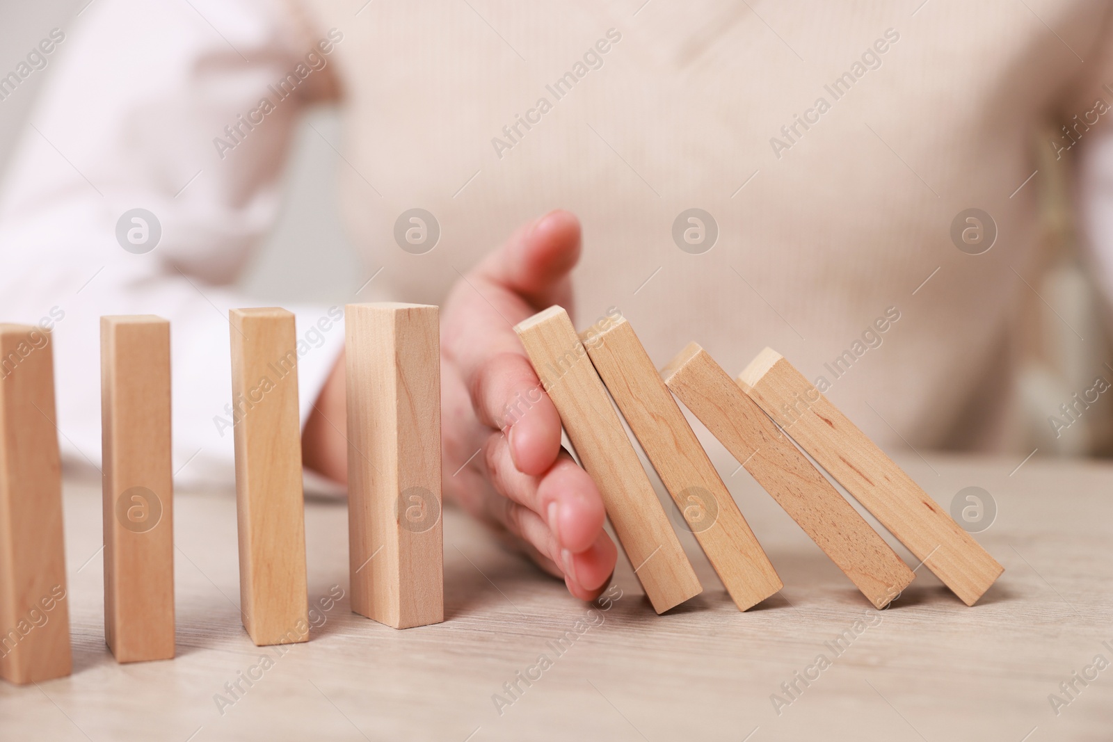 Photo of Woman stopping wooden blocks from falling at table, closeup. Domino effect