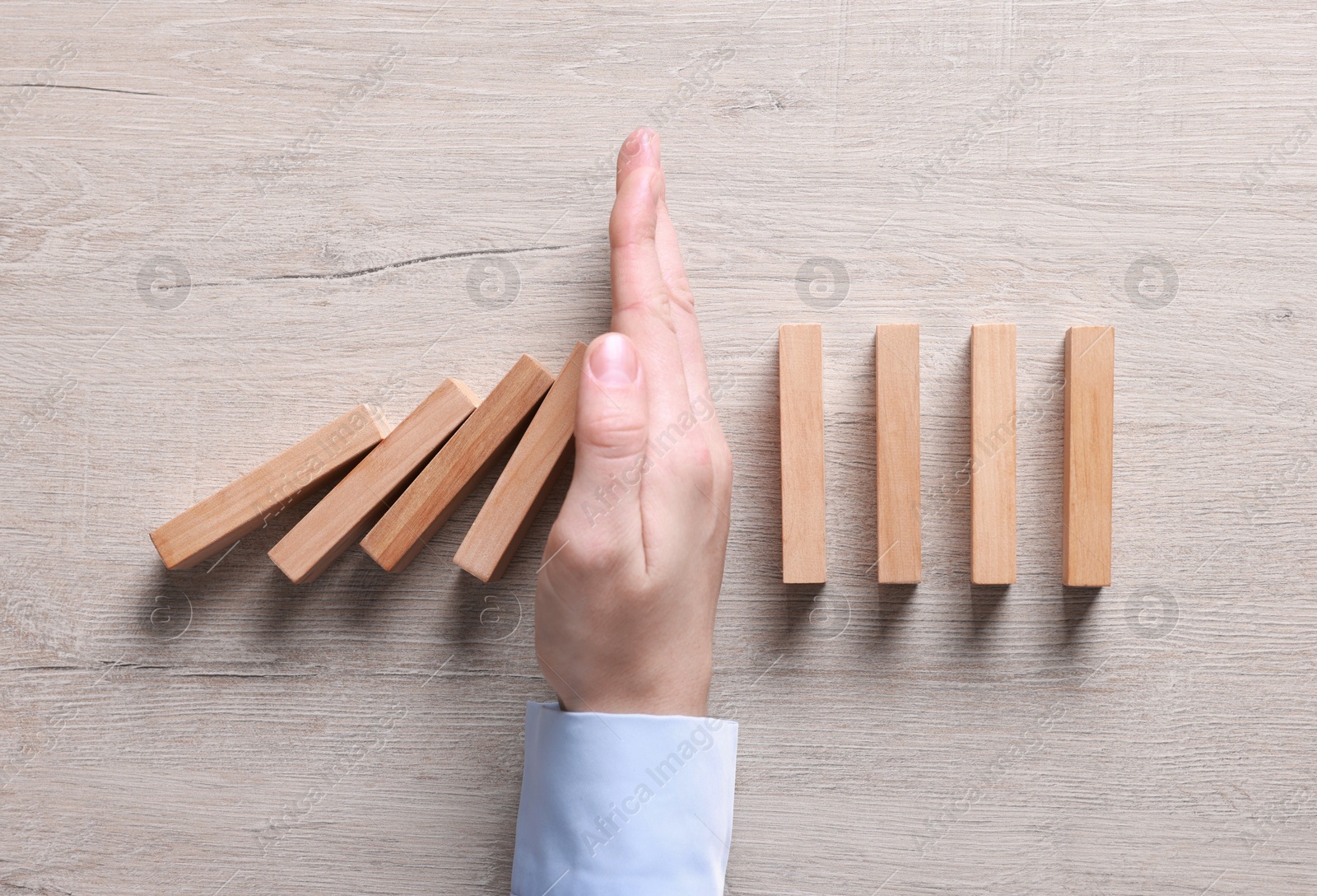 Photo of Man stopping wooden blocks from falling at table, top view. Domino effect