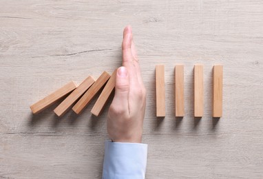 Photo of Man stopping wooden blocks from falling at table, top view. Domino effect