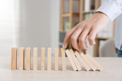 Photo of Man stopping wooden blocks from falling at table, closeup. Domino effect