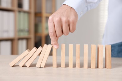 Photo of Man stopping wooden blocks from falling at table, closeup. Domino effect