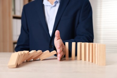 Photo of Man stopping wooden blocks from falling at table, closeup. Domino effect