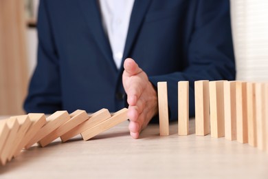 Photo of Man stopping wooden blocks from falling at table, closeup. Domino effect