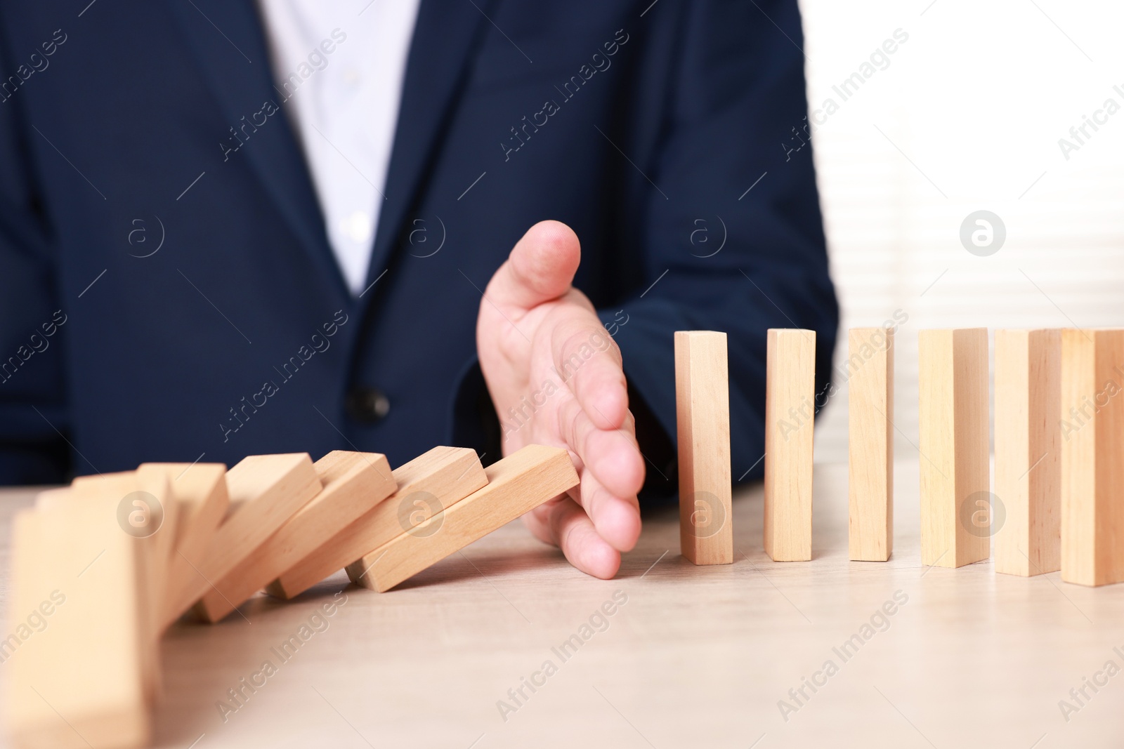 Photo of Man stopping wooden blocks from falling at table, closeup. Domino effect