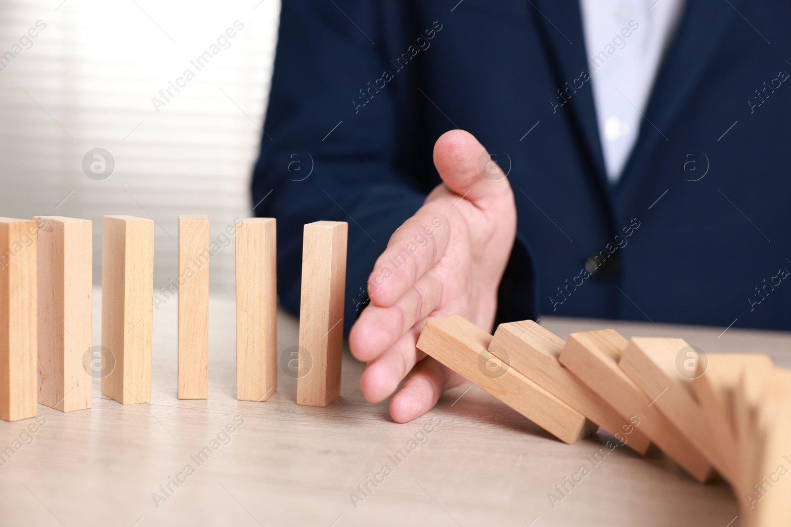 Photo of Man stopping wooden blocks from falling at table, closeup. Domino effect