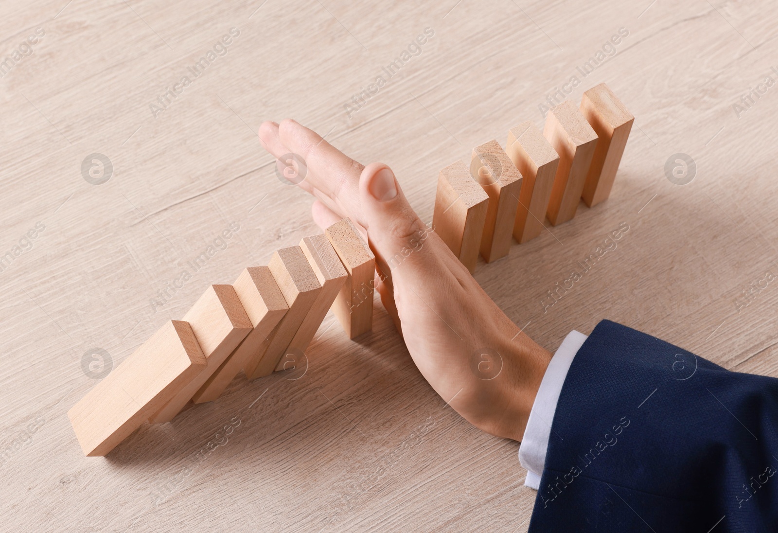 Photo of Man stopping wooden blocks from falling at table, closeup. Domino effect