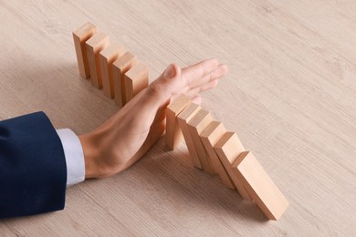 Photo of Man stopping wooden blocks from falling at table, closeup. Domino effect