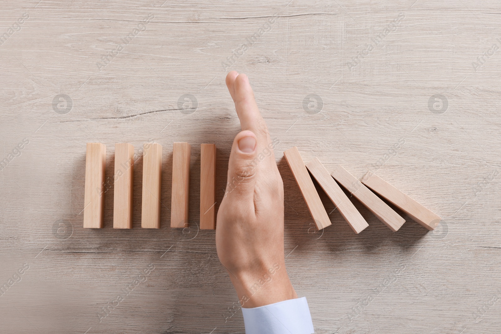 Photo of Man stopping wooden blocks from falling at table, top view. Domino effect