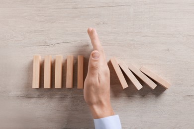 Photo of Man stopping wooden blocks from falling at table, top view. Domino effect