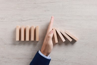 Photo of Man stopping wooden blocks from falling at table, top view. Domino effect