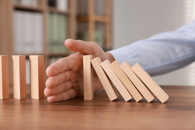 Photo of Man stopping wooden blocks from falling at table, closeup. Domino effect