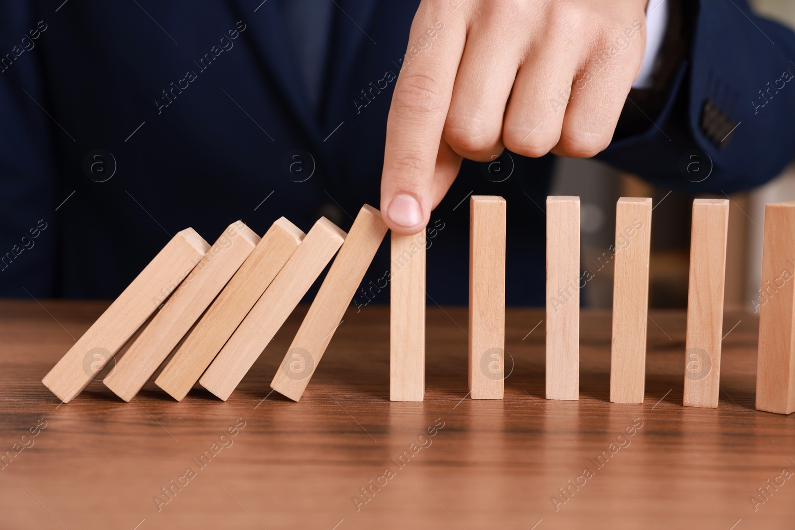 Photo of Man stopping wooden blocks from falling at table, closeup. Domino effect