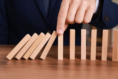 Photo of Man stopping wooden blocks from falling at table, closeup. Domino effect