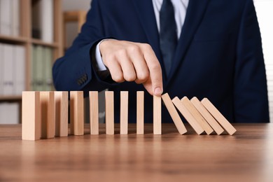 Photo of Man stopping wooden blocks from falling at table, closeup. Domino effect