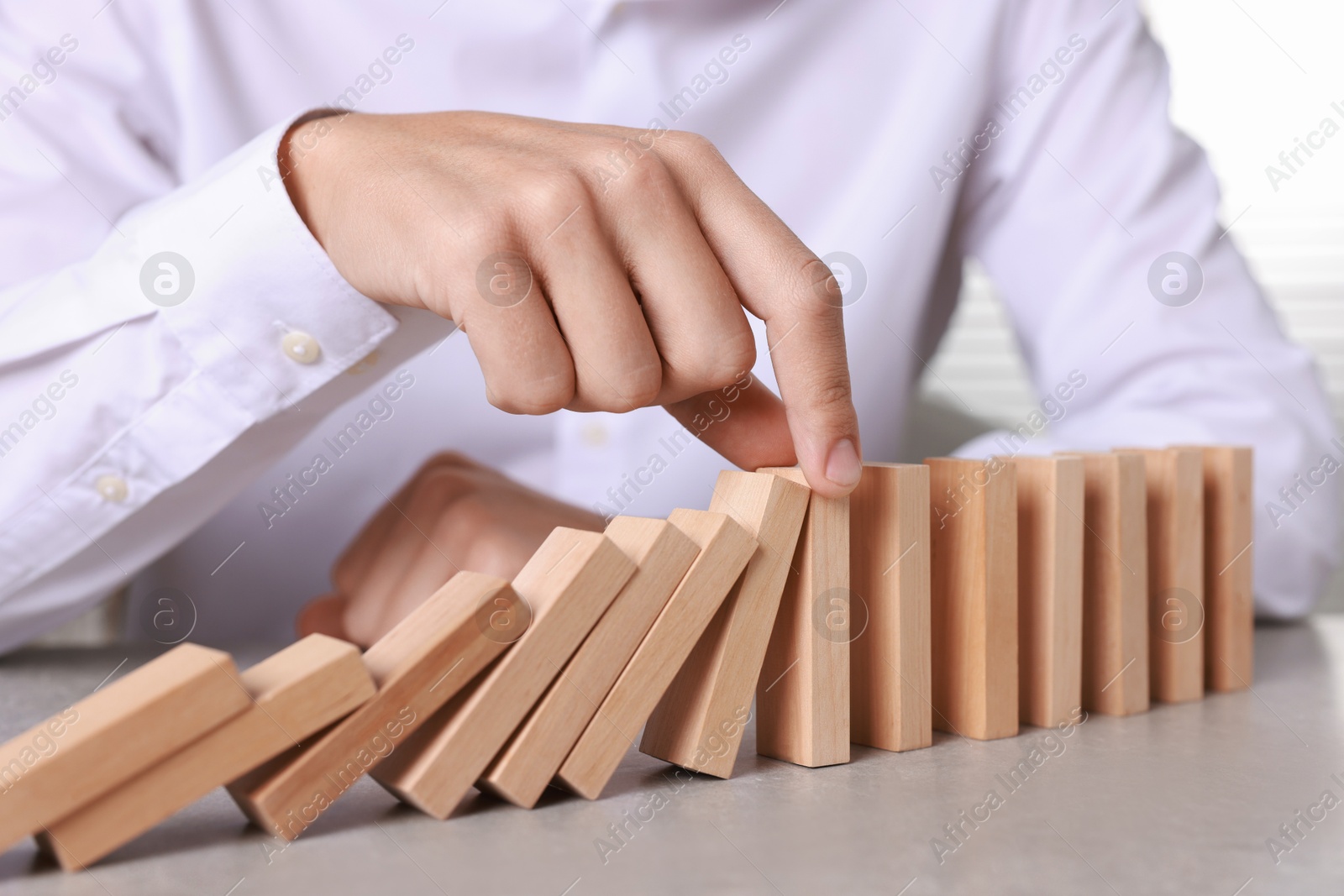 Photo of Man stopping wooden blocks from falling at table, closeup. Domino effect