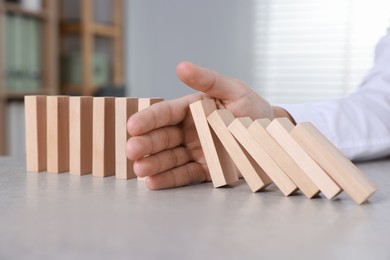 Photo of Man stopping wooden blocks from falling at table, closeup. Domino effect