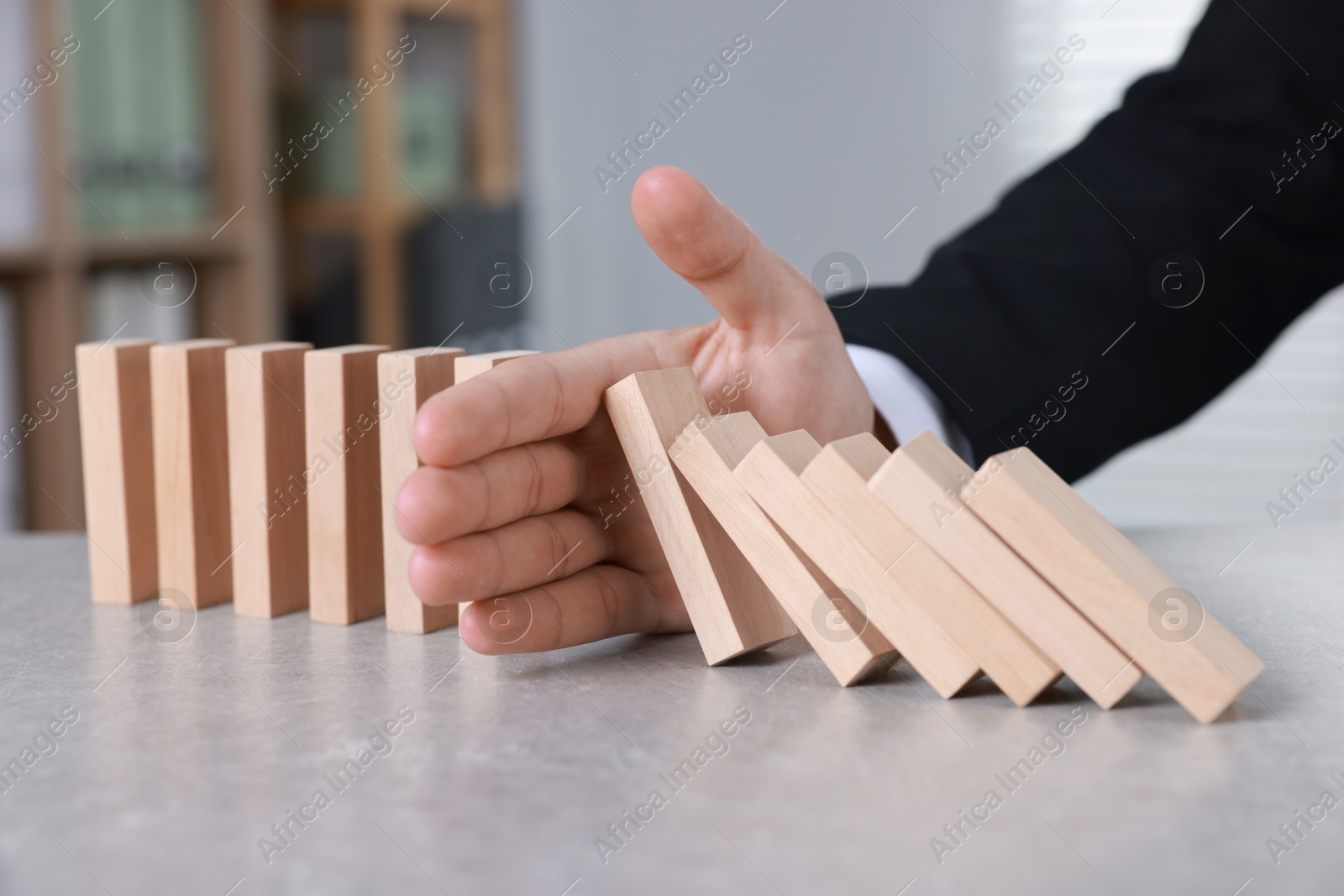 Photo of Man stopping wooden blocks from falling at table, closeup. Domino effect