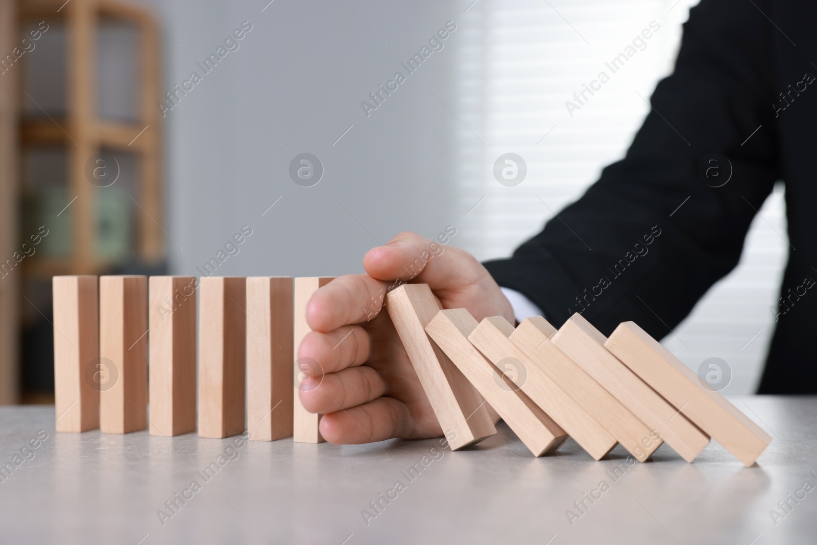 Photo of Man stopping wooden blocks from falling at table, closeup. Domino effect