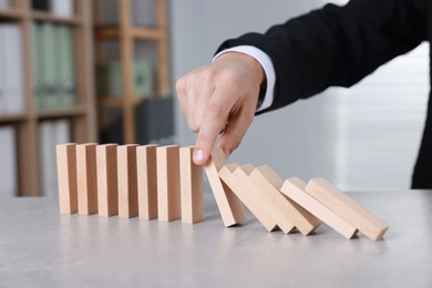 Photo of Man stopping wooden blocks from falling at table, closeup. Domino effect