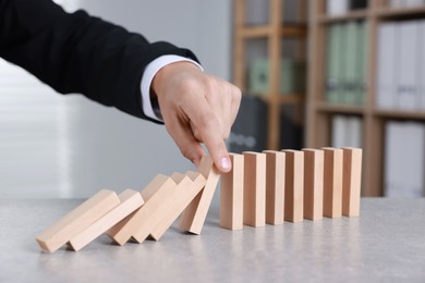 Photo of Man stopping wooden blocks from falling at table, closeup. Domino effect