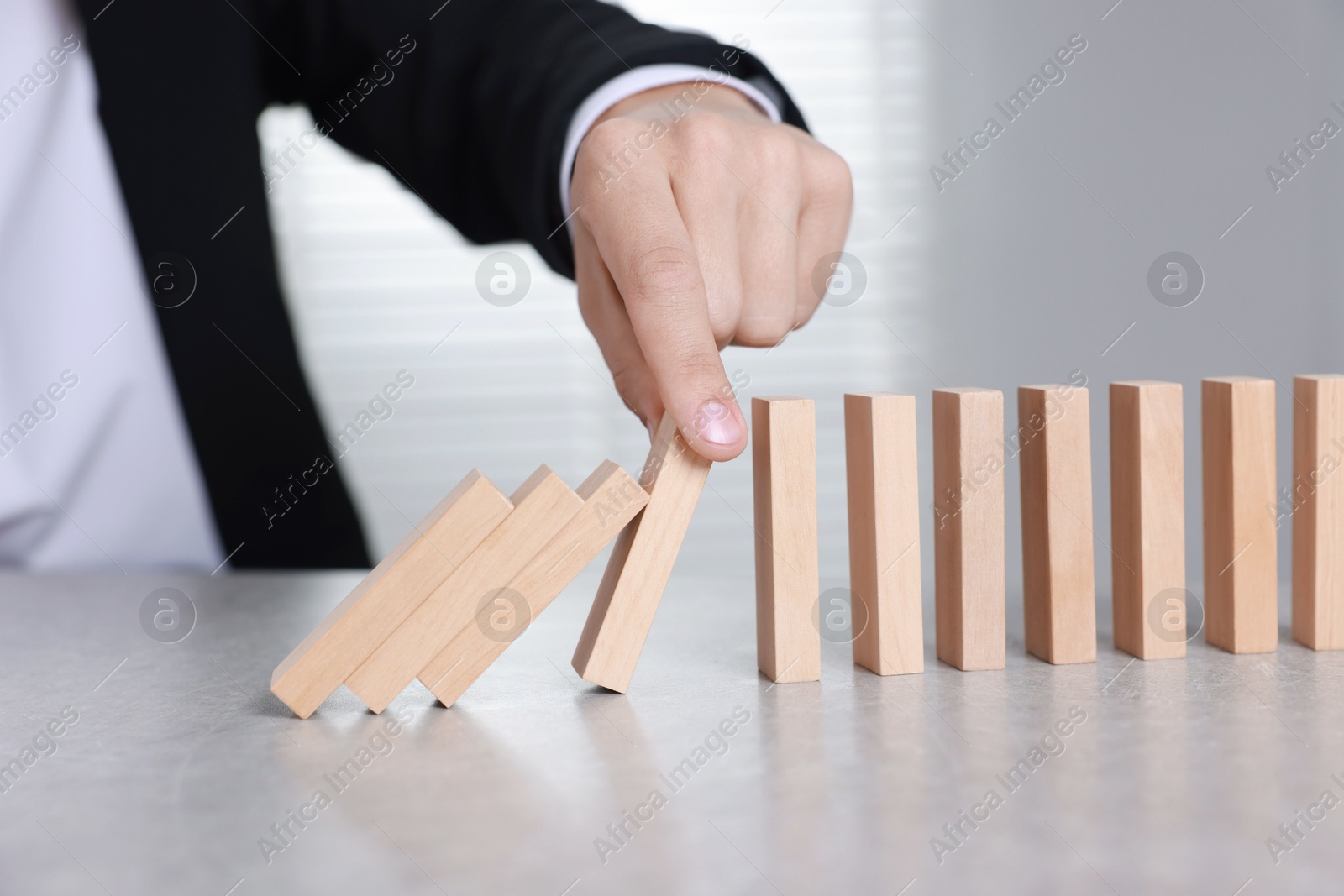 Photo of Man stopping wooden blocks from falling at table, closeup. Domino effect