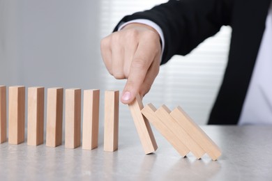 Photo of Man stopping wooden blocks from falling at table, closeup. Domino effect