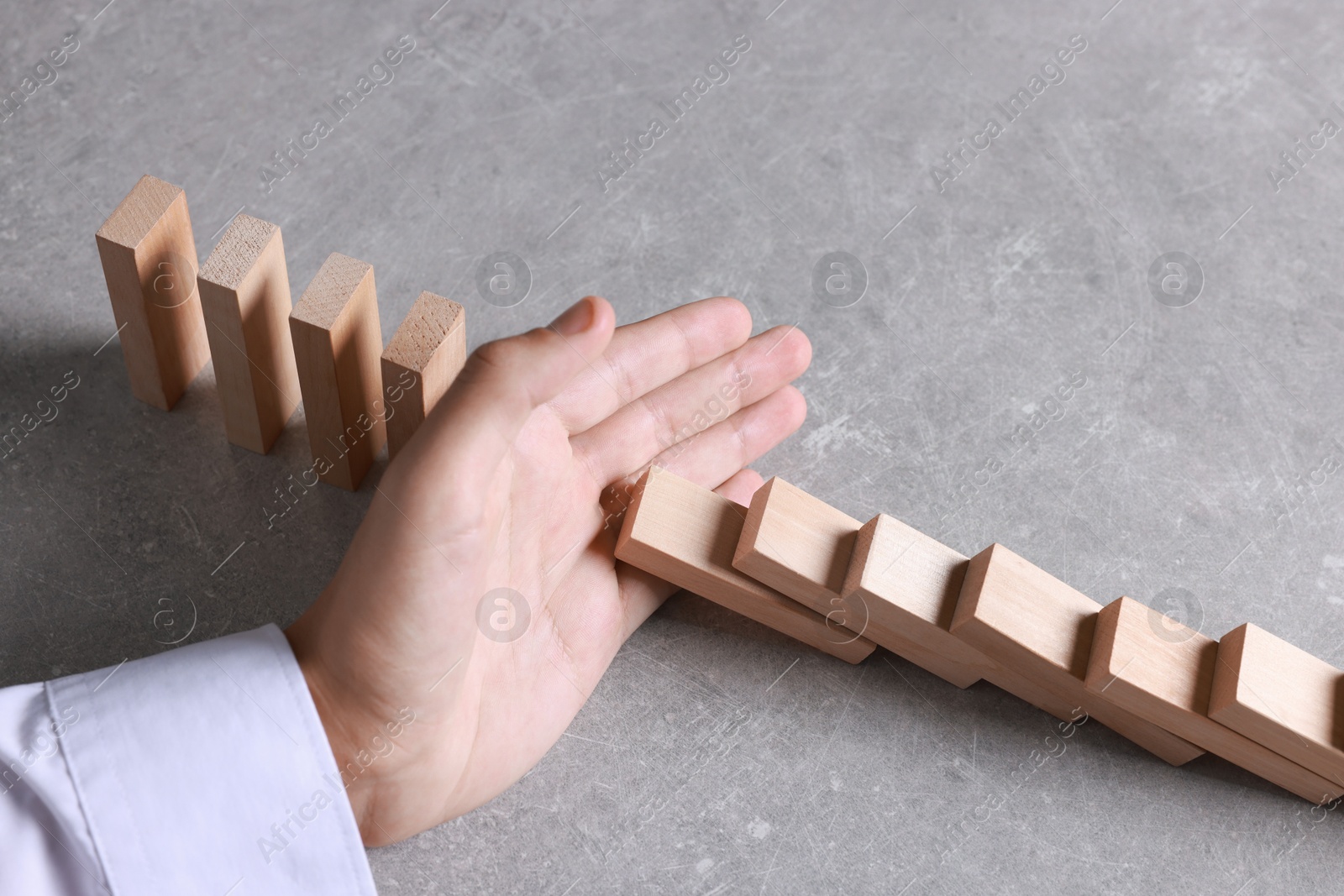 Photo of Man stopping wooden blocks from falling at table, closeup. Domino effect