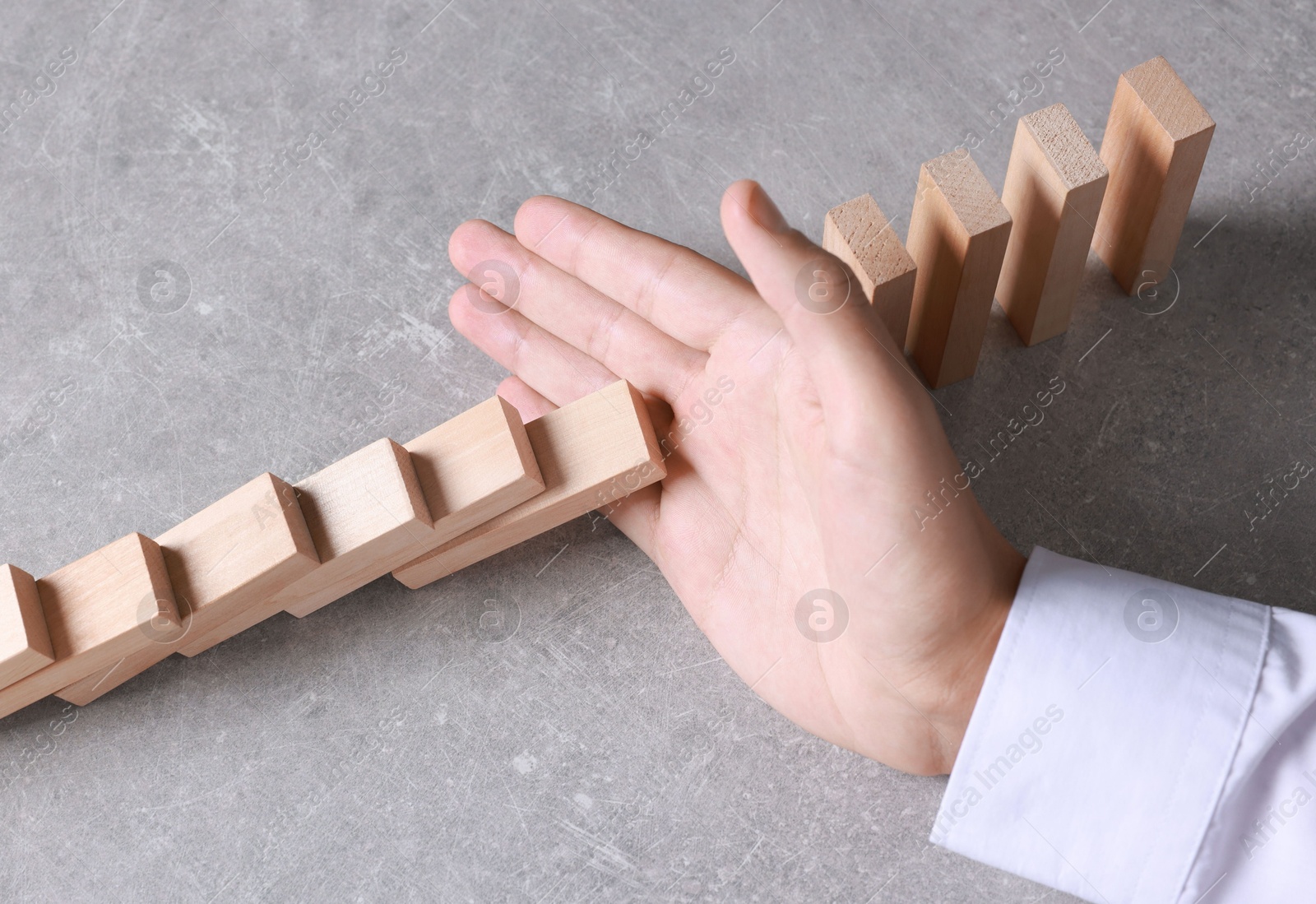 Photo of Man stopping wooden blocks from falling at table, closeup. Domino effect